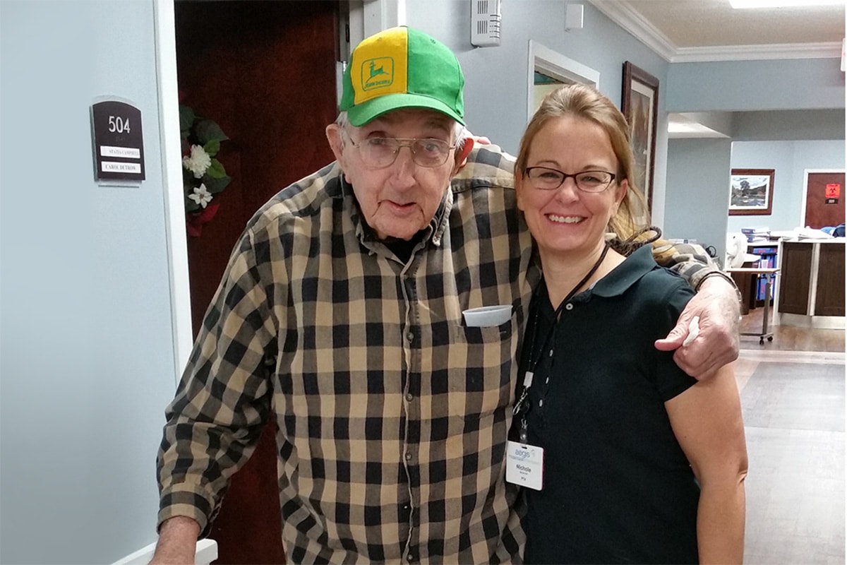 An elderly resident with a caregiver standing in the hallway at Richwood Nursing