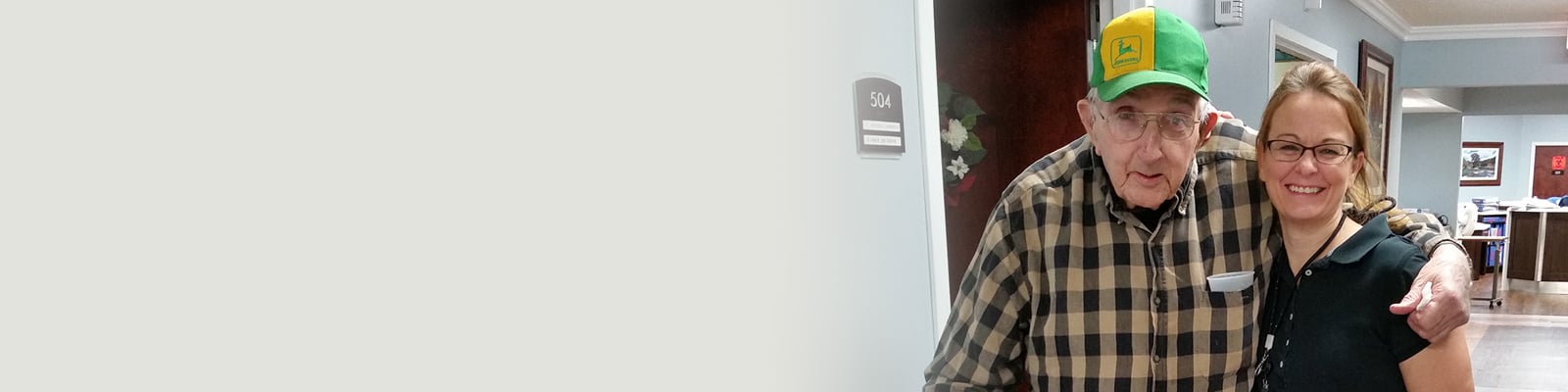 An elderly resident with a caregiver standing in the hallway at Richwood Nursing